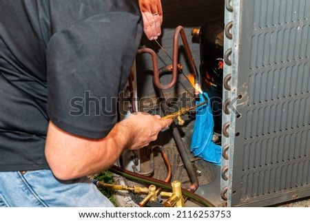 Maintenance worked uses and oxygen Acetylene torch to braze copper tubing on an air conditioner system Royalty-Free Stock Photo #2116253753