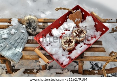 cups of cappuccino and wooden heart placed in  a red tray with snow on old  wooden sled with a hat 