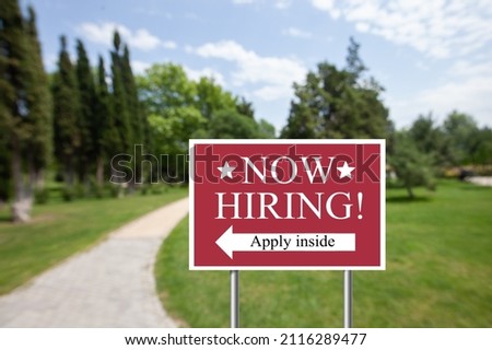 Outdoor lawn sign now hiring apply inside with a direction arrow. Employment, understaffed business