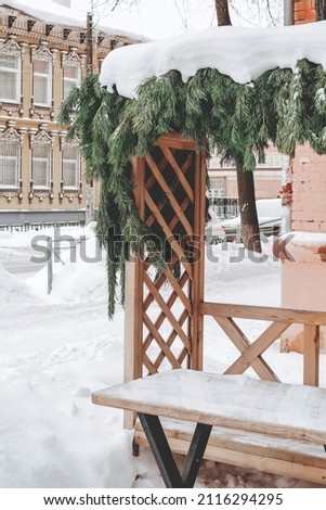 Wooden besdka decorated with green branches of spruce. Snowy romantic gazebo in winter
