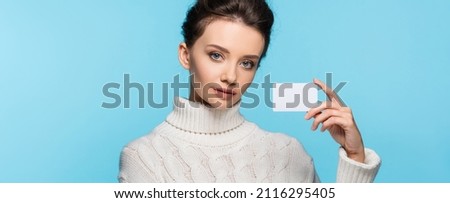 Brunette model in knitted sweater holding blank card isolated on blue, banner