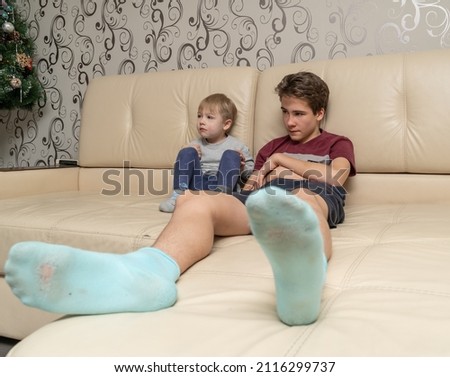 Two brothers are sitting on the sofa watching a movie 3 years old and 13 years old. A small blond German child is a big Caucasian guy.
