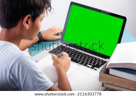 student using green screen on computer and writing on diary with some books on table