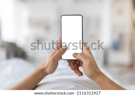 Mobile Mockup. Unrecognizable Male Holding Blank Smartphone With White Screen While Relaxing In Bed At Home, Man Using Empty Mobile Phone With Copy Space For App Or Website Design, POV Shot Royalty-Free Stock Photo #2116312427