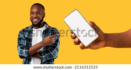 Recommendation. Portrait of cheerful black guy pointing finger at big blank cell phone screen, hand holding device with white empty display. Gadget with free space for mock up, banner panorama