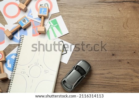 Many different road signs, notebook and toy car on wooden background, flat lay with space for text. Driving school