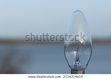 Close-up of a standard E14 40W incandescent transparent candle light bulb, on a background of water and defocused sky at sunset Royalty-Free Stock Photo #2116314614