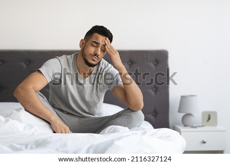 Fatigue Concept. Tired Young Arab Man Sitting In Bed At Home, Exhausted Millennial Middle Eastern Guy Waking Up In Bedroom, Feeling Unwell, Having Headache Or Suffering Insomnia, Free Space Royalty-Free Stock Photo #2116327124