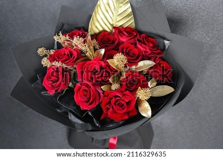 Bouquet of red roses with golden decorative branches in a black package Royalty-Free Stock Photo #2116329635