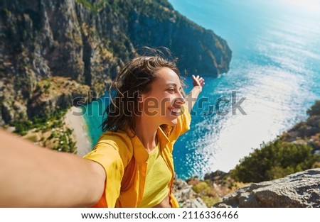 Positive tourist woman taking picture outdoors for memories, making selfie on top of cliff with valley mountains view, sharing travel adventure journey Royalty-Free Stock Photo #2116336466