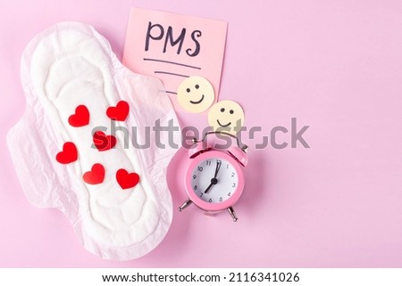 Women's Menstrual pads (sanitary napkin) with red hearts, PMS inscription, funny emoticons, an alarm clock on pink background. The concept of the time of critical days, women's health. Space for text Royalty-Free Stock Photo #2116341026