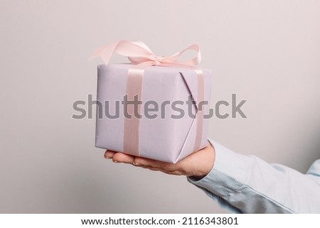 Close up shot of woman hands holding gift package box on pink pastel background with copy space.