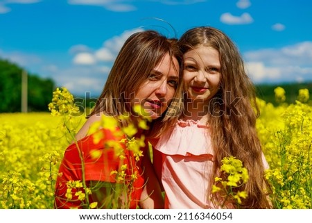 Mom and daughter in nature outdoors lifestyle. Cheerful lightning yellow color of blooming rapeseed field on the background. The concept of a good holiday.