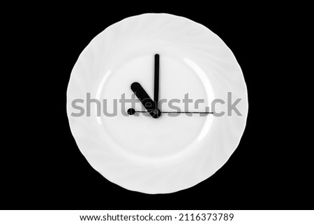 Lunch time clock. plate with clock. clock hands on white dish.  black background. eleven o'clock Royalty-Free Stock Photo #2116373789