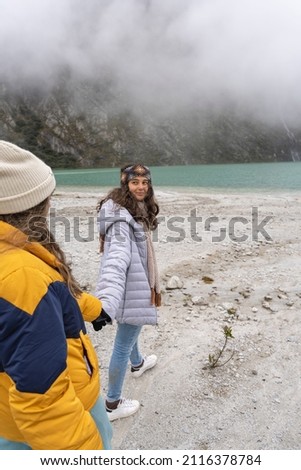 Vertical photo of a young couple holding hands while walking next to Llanganuco lagoon in Peru