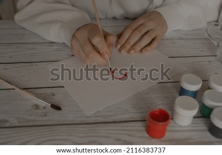 The girl draws a heart on a white sheet with red paint. Gouache drawing.