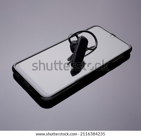 The Bluetooth headset is on the smartphone screen. gadgets lie on a reflective surface. copy space.