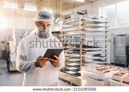 A food factory worker using tablet and checking on cookies.