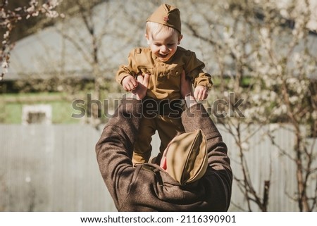 9th May. A Soviet soldier throws a little boy in a military uniform up. The concept of the Great Victory Day 1941-1945 and Defender of the Fatherland Day. Royalty-Free Stock Photo #2116390901