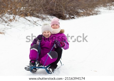 Satisfied happy cheerful children girls sisters siblings sledding down the mountain. Winter activities outside