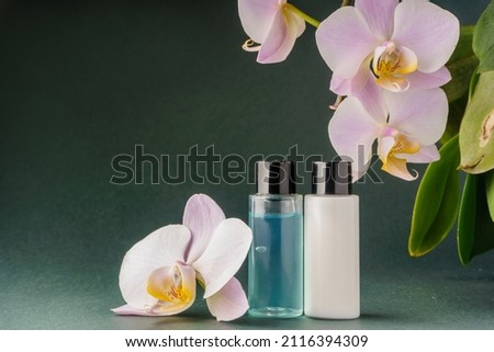 Shower gel and shampoo in small bottle, black lid on a green background with orchid. High quality photo