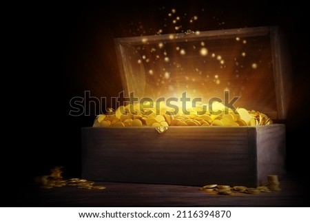 Open treasure chest with gold coins on wooden table against black background Royalty-Free Stock Photo #2116394870