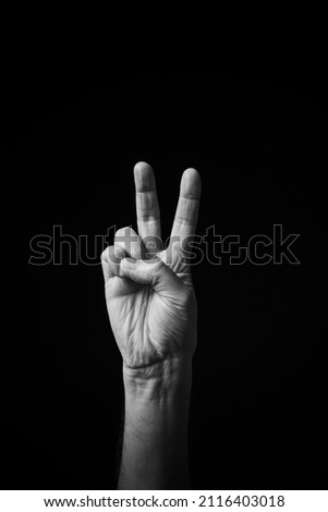 Dramatic black and white  image of a male hand fingerspelling the Chinese sign language letter 'V', isolated against a dark background.