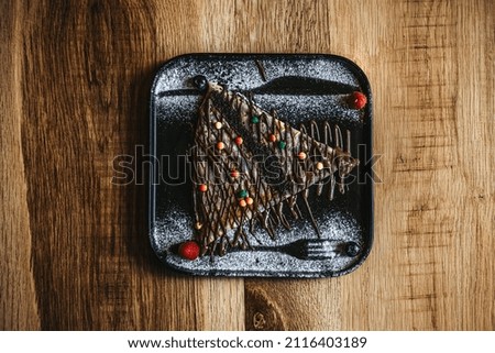 this picture represents a crepe with chocolate and candies on a black plate