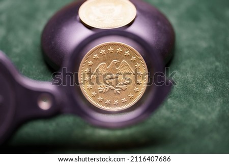 Golden coin under a magnifying glass on a green cloth 