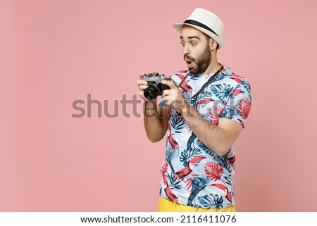 Shocked young traveler tourist man in summer clothes hat hold retro vintage photo camera isolated on pink background studio portrait. Passenger traveling abroad on weekend. Air flight journey concept