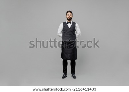 Full body confident young barista male waiter butler man 20s wear white shirt vest elegant uniform work at cafe looking camera isolated on plain grey background studio. Restaurant employee concept. Royalty-Free Stock Photo #2116411403
