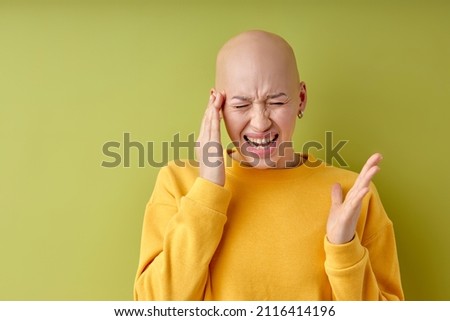 Bald annoyed caucasian lady touching head with fingers, suffering from headache. isolated on green studio background, unhappy angry hairless female screaming, migraine, cancer concept