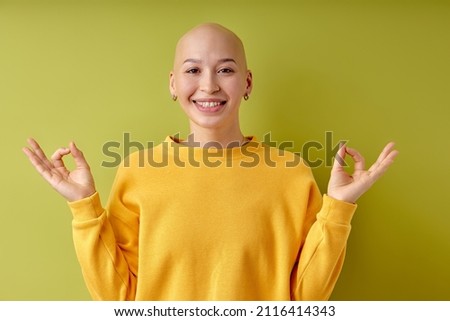 Keep calm, yoga. Happy young caucasian bald woman isolated on green studio background. Beautiful excited female model. Human emotions, facial expression, sales, ad concept. Youth
