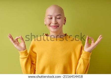 Keep calm, yoga. Portrait of young caucasian bald woman isolated on green studio background. Charming hairless female model with eyes closed. Human emotions, facial expression, sales, ad. Youth