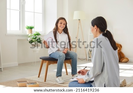 Don t be afraid to talk about emotions. Happy teen girl in meeting with professional child psychologist talks about emotions. Cheerful girl shows female psychologist painted smiling smiley.