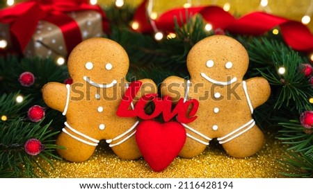 Two gingerbread men, the word LOVE and red heart on glitter golden background. Concept for Valentine's day. Close-up.