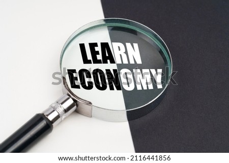 Business concept. On the surface, which is half black and white, lies a magnifying glass inside which is written - LEARN ECONOMY