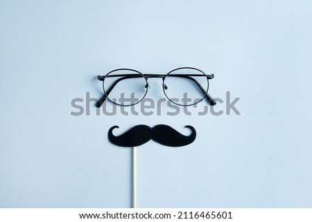 Father's Day Holiday Concept. Transparent glasses, stylish black paper photo booth props moustaches on blue background.  Royalty-Free Stock Photo #2116465601