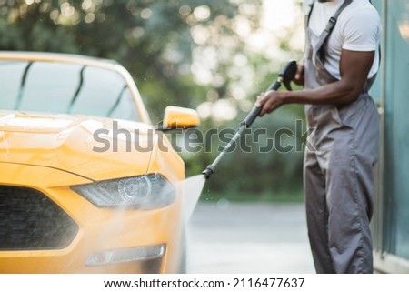 Close up cropped horizontal image of hands of African man washing his yellow luxury car using high pressure water, at outdoors car self washing service. Royalty-Free Stock Photo #2116477637