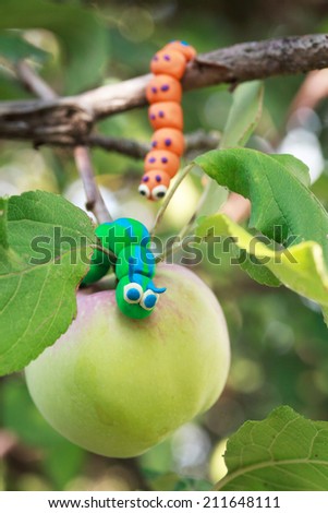 Plasticine world - little homemade green and orange caterpillars is crawling on the apple, selective focus on first