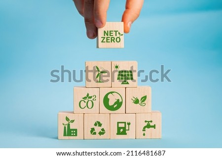 Net zero and carbon neutral concept. Net zero greenhouse gas emissions target. Climate neutral long term strategy. Hand put wooden cubes with green net zero icon and green icon on grey background. Royalty-Free Stock Photo #2116481687