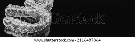 Banner with dental teeth aligners or invisible braces for straightening teeth on the black background with copy space. Orthodontic devices for the perfect smile.