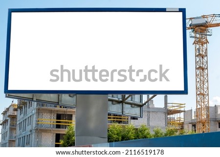 Blank white billboard for advertisement near the construction site with tower cranes