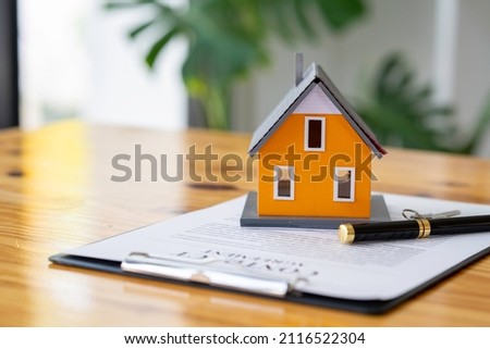 Model houses and contract documents on the desk in the office to decide to sign a home insurance contract about mortgage and home insurance offers Royalty-Free Stock Photo #2116522304