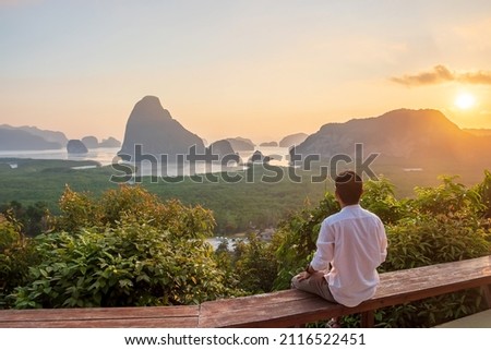 Happy traveler man enjoy Phang Nga bay view point, alone Tourist sitting and relaxing at Samet Nang She, near Phuket in Southern Thailand. Southeast Asia travel, trip and summer vacation concept Royalty-Free Stock Photo #2116522451