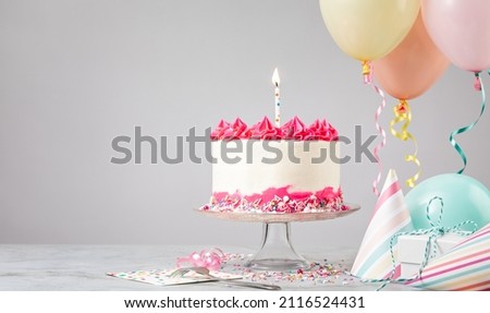 Pink Birthday cake with candle, presents, hats and colorful balloons over light grey background. Birthday Party!