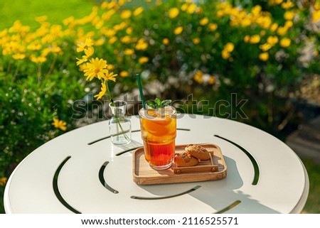 fresh homemade peach ice tea with mint, chocolate chip cookie served on table outdoors. summer cold fruit drink in sunny afternoon with yellow flowers behind Royalty-Free Stock Photo #2116525571