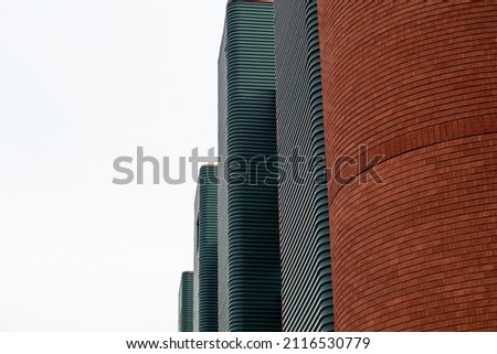 Green metal exterior wall panels with small symmetric line patterns running horizontally on multiple panels. The tall red brick wall is curved and circular in design. The background is white.