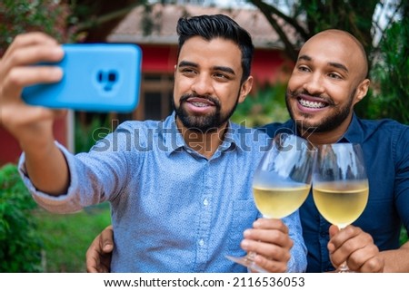 black gay couple taking selfie with mobile and glass of wine outside in the garden