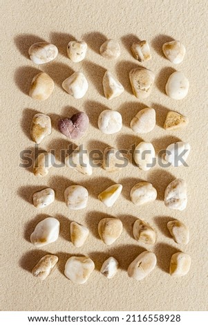 Pattern with different pebble sea stones and one stone heart on fine sand. Square composition from natural rocks neutral beige color. Spa minimal background, concept for meditation and love, flat lay